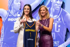 An image of Caitlin Clark and someone from the WNBA Office holding Clark's new Indiana Fever jersey after she was drafted.