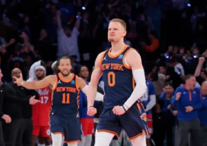 An image of Donte DiVincenzo flexing after hitting the go ahead three pointer in Game 2. Jalen Brunson is celebrating in the background.