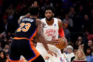 A picture of Joel Embiid being guarded by Mitchell Robinson. Knicks are wearing their black jerseys, and Philadelphia is wearing their alternate white jerseys. 