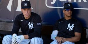 An image of Aaron Judge and Juan Soto sitting in the Yankees dugout, with their navy Yankees pullovers on.