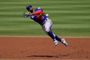 An image of Francisco Lindor falling over while throwing a ball to first base. He is wearing the Mets road Blue uniforms.